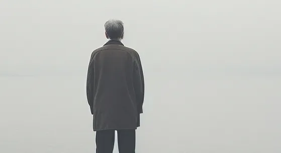 Wide misty seascape with an elderly figure seen from behind.
