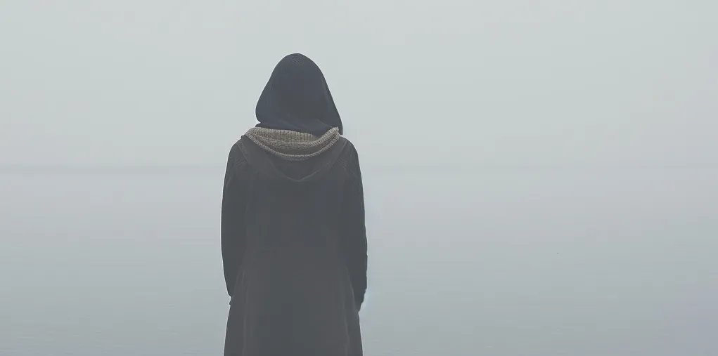 Wide misty seascape with a figure wearing a hijab seen from behind.