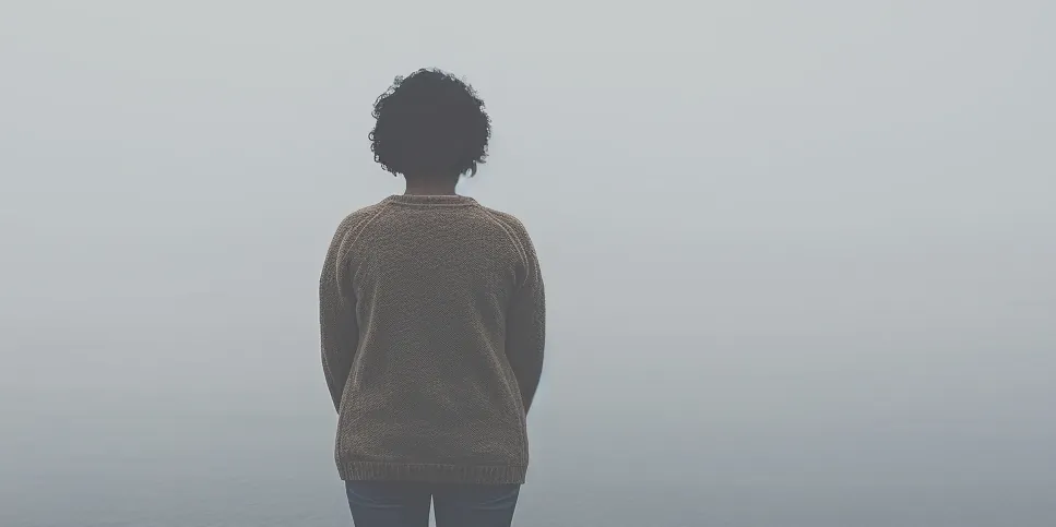 Wide misty seascape with a young figure seen from behind.